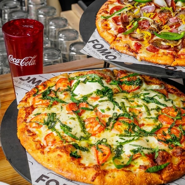 Two pizzas, one with vegetables and another with tomatoes and basil, with drinks on a table.