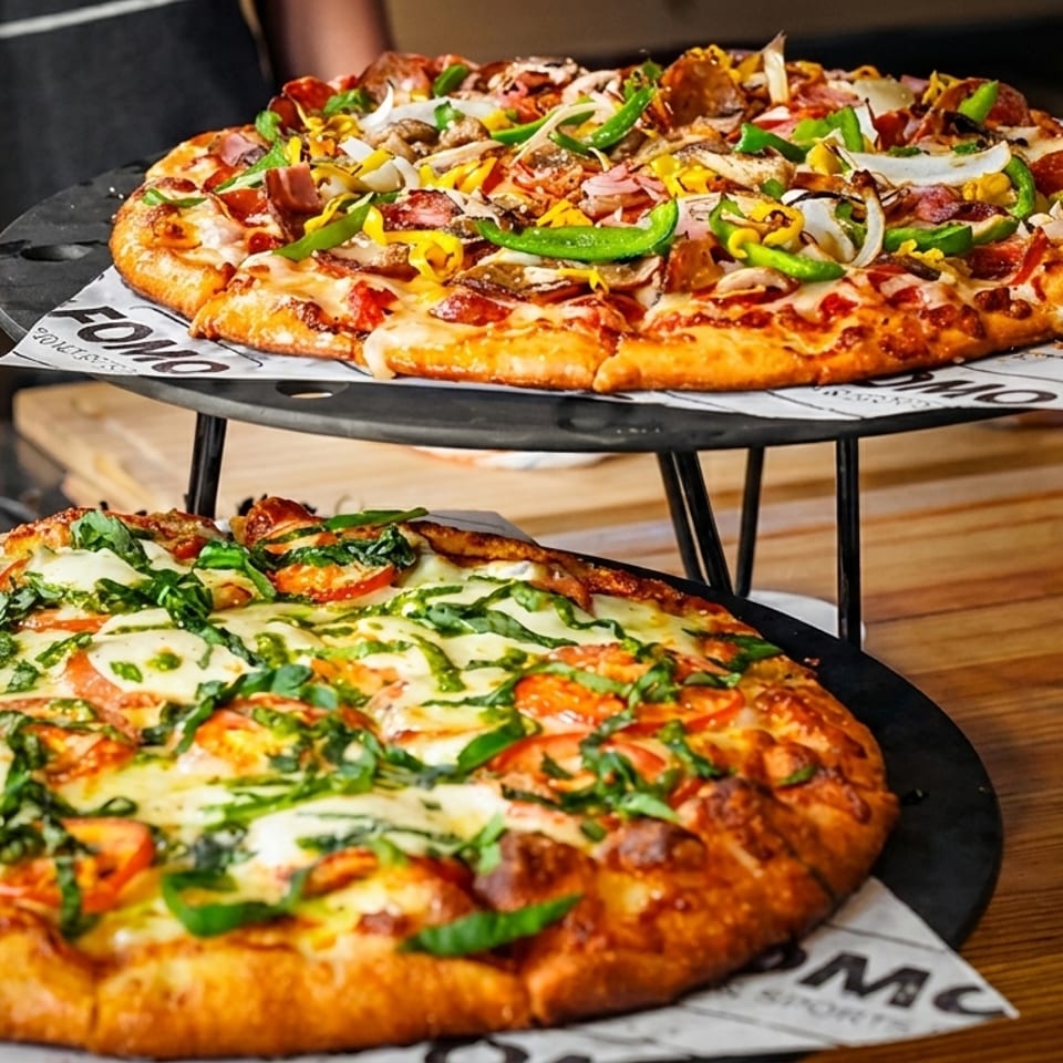 Two delicious pizzas, one with pesto and tomatoes, the other with various toppings, on a wooden table.